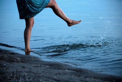 Low section of woman splashing water in sea at beach