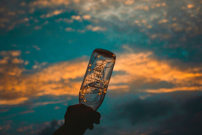 Close-up of hand holding glass against sky during sunset