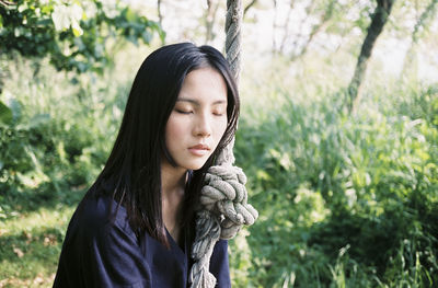 Beautiful young woman sitting on swing at forest