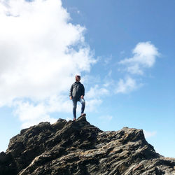 Low angle view of man standing on rock against sky