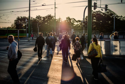 Rear view of people crossing street in city during sunset