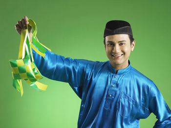 Man in traditional clothing holding decorations against green background