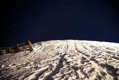 Snow covered land against sky at night