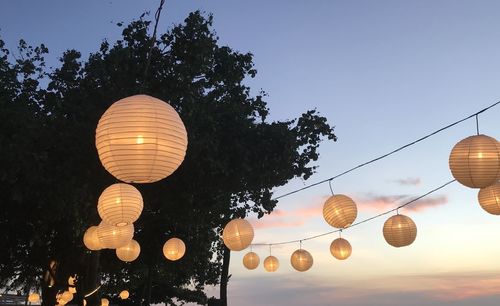 Low angle view of illuminated lanterns hanging against sky at dusk