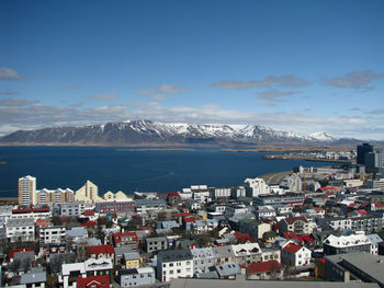 High angle view of townscape by sea with snowcapped mountains in the background