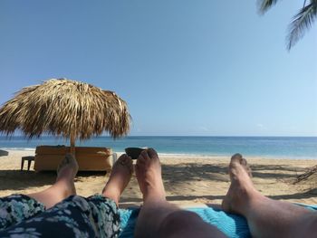 Low section of people relaxing on beach against clear sky