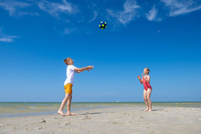 Full length of friends playing on beach against sky