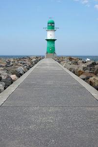 Empty pier leading towards lighthouse by sea against sky