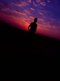 Silhouette man standing on landscape against sky at sunset