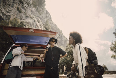 Young male and female friends discussing while unloading luggage from van trunk