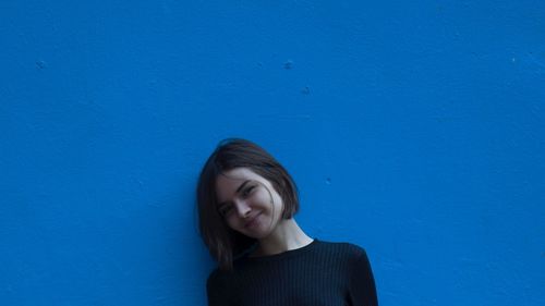 Portrait of young woman smiling while standing by blue wall