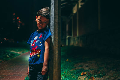 Portrait of boy leaning against pole at night