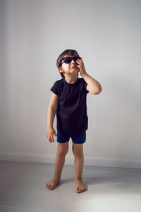 Boy in a black t-shirt stands at home against the background of a white room in sunglasses 