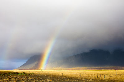 Majestic view of rainbow over landscape amidst cloudy sky