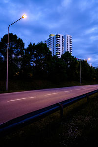 Empty road by buildings against sky in city