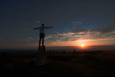 Silhouette man standing on field against sky during sunset