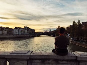 Rear view of man sitting on river against sky