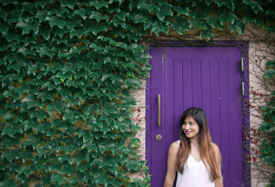 Smiling woman standing against closed door by plants