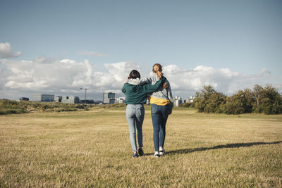 Rear view female friends with arms around standing in park