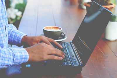 Midsection of man holding coffee cup on table