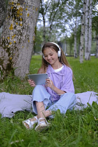 A teenage girl sits on the lawn in the park and holds a planchette in her hands