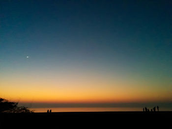 Silhouette people walking on beach against clear sky at sunset