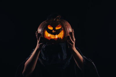 Midsection of woman holding pumpkin against black background