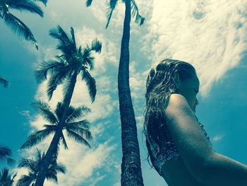 Low angle view of girl standing by palm tree against sky at beach