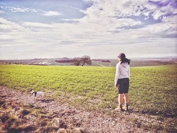 Rear view of woman standing with jack russell terrier on field against cloudy sky