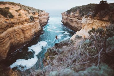 Rear view of woman standing on cliff against sea