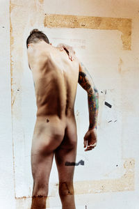 Rear view of shirtless man standing against wall