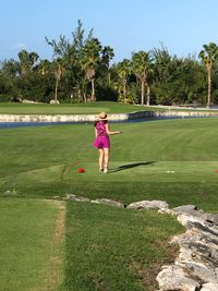 Rear view of woman playing golf on course against trees