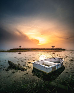 Boat moored on beach against sky during sunset