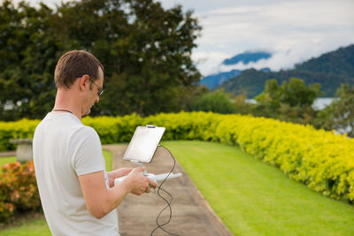 Young man holding drone remote drone on walkway at park