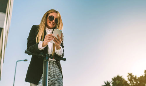 Young woman using smart phone against sky