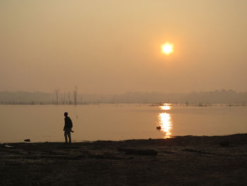 Silhouette man standing by lake against sky during sunset