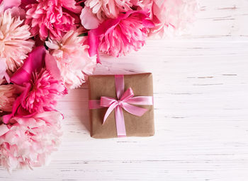 A gift wrapped in kraft paper, a pink ribbon and a bouquet of pink peonies on a white background