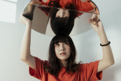 Young woman holding mirror against wall