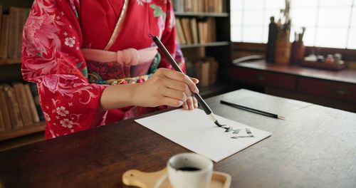 Midsection of woman writing in book at table