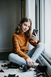 Young woman using smart phone while sitting on laptop