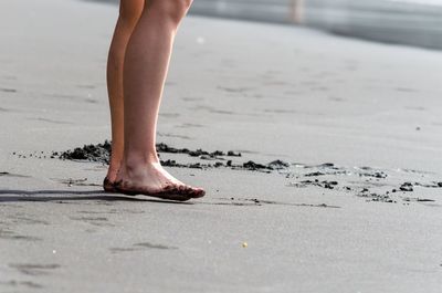 Low section of woman standing at shore of beach