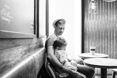 Father sat cuddling his son whilst drinking coffee in a cafe