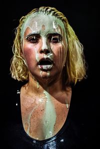 Close-up portrait of young woman with messy face against black background