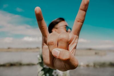 Man showing horn sign while standing against sky