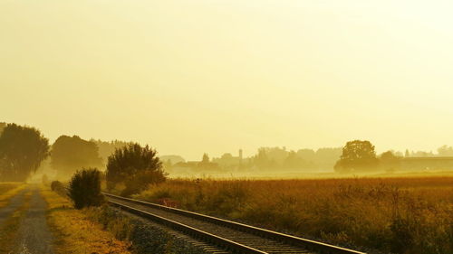 Dirt road amidst field against sky during sunset