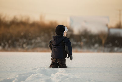 Boy wearing warm clothing while standing on snowy field during sunset