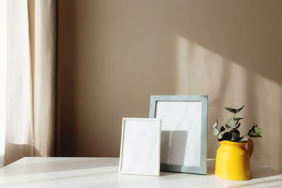 A yellow ceramic jug or vase with eucalyptus branches, empty white photo frames on the white table
