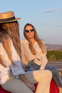 Portrait of young smiling and laughing women sitting on classic red car at sunset with orange light