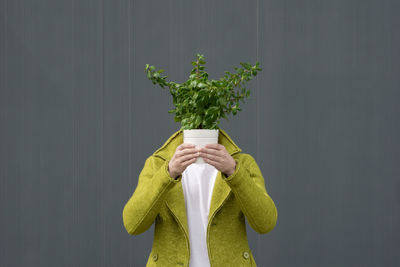 Close-up of person with potted plant against grey background