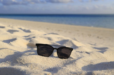 Close-up of sunglasses on sand at beach against sky